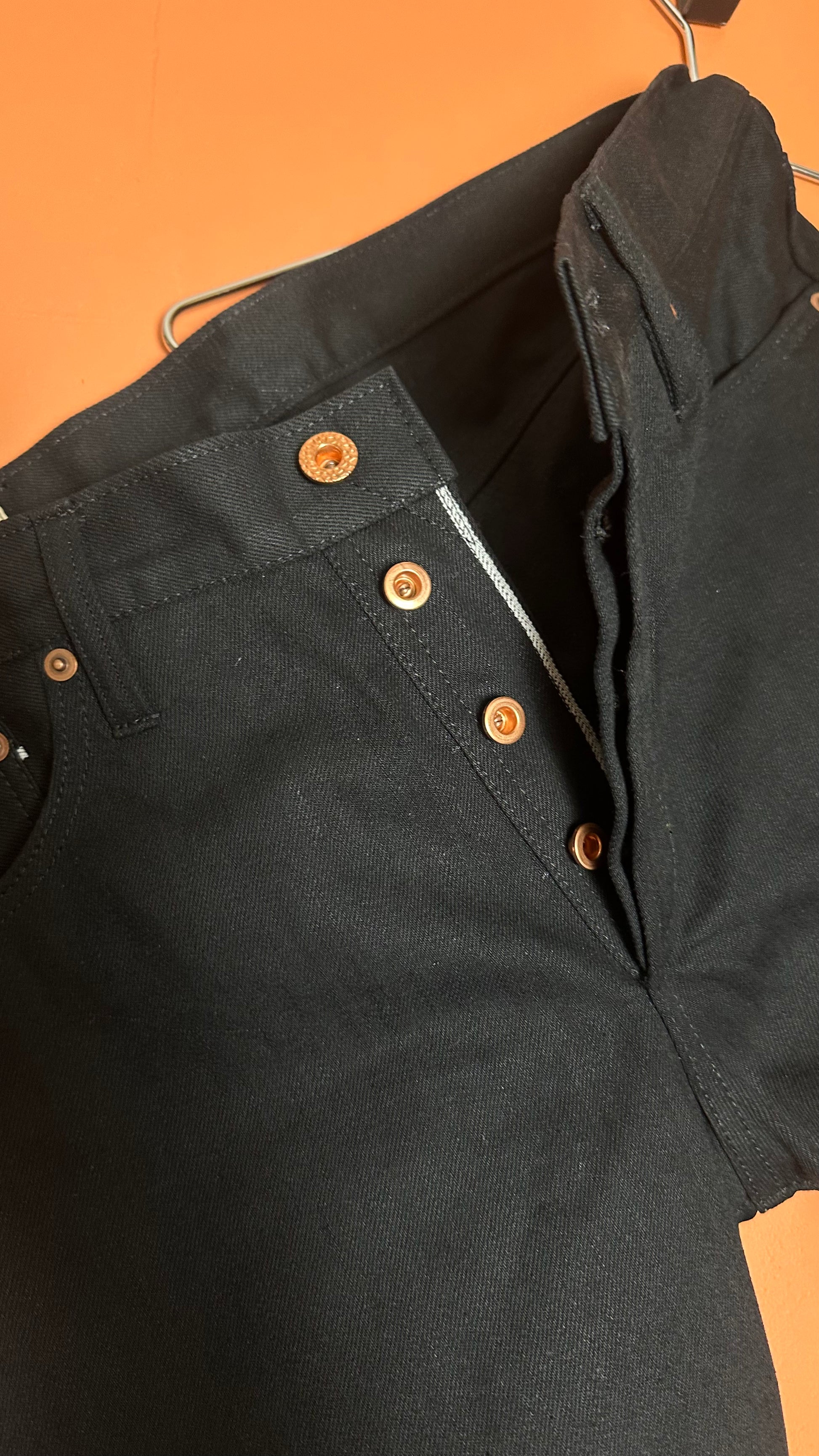 Black jacket with gold buttons on a hanger against an orange background