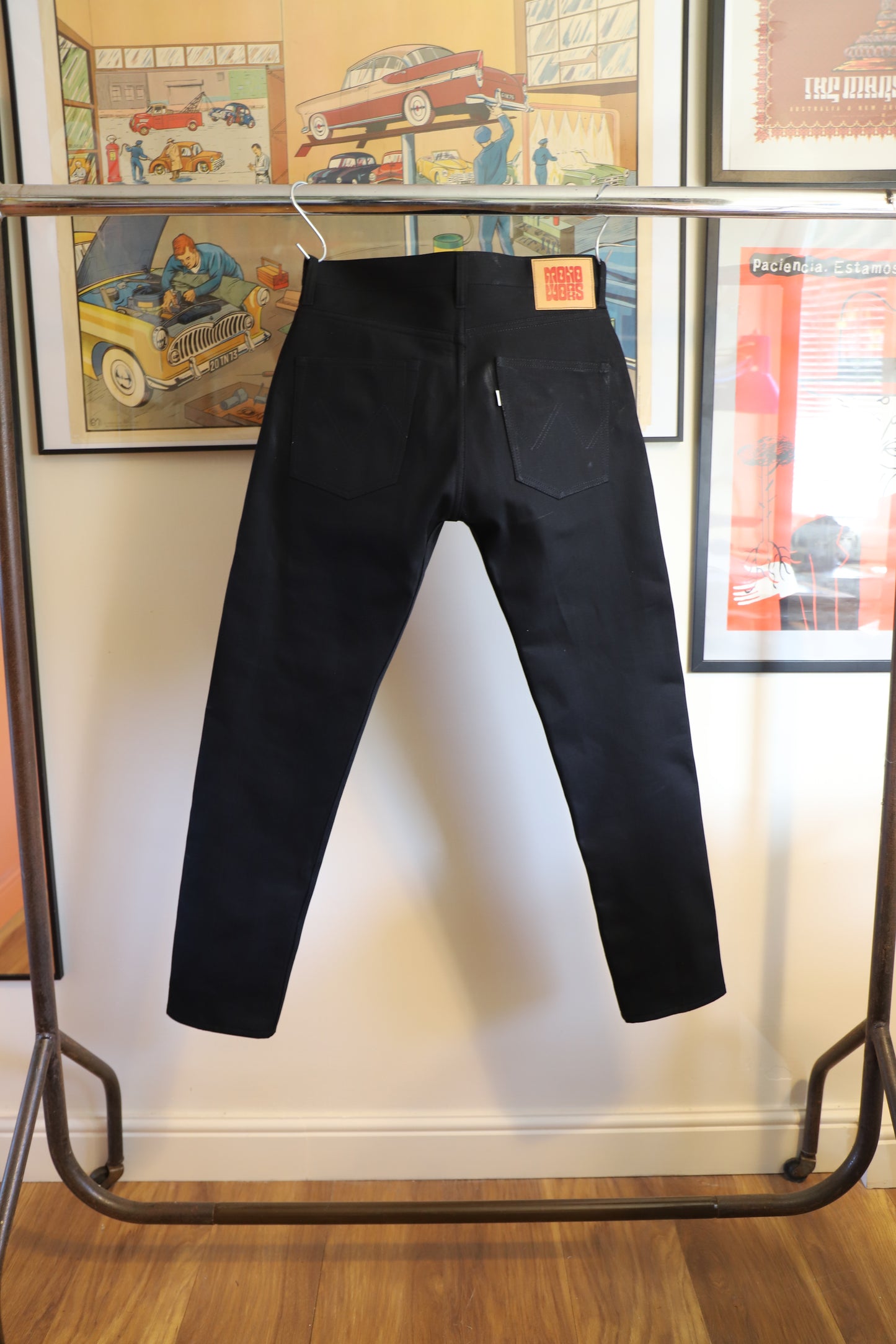 Black pants displayed on a rack with a wooden floor and framed pictures in the background