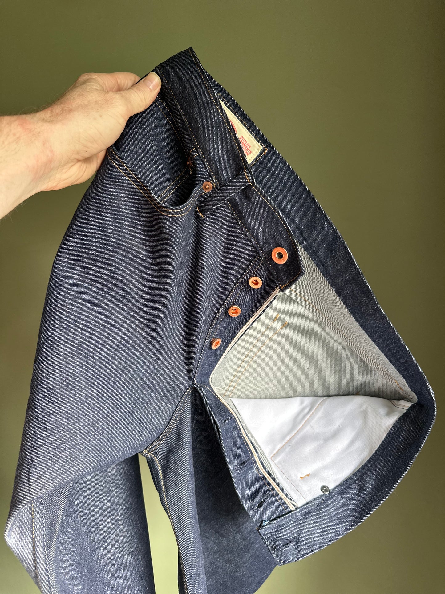Blue denim jeans with orange buttons held open by a hand on a green background