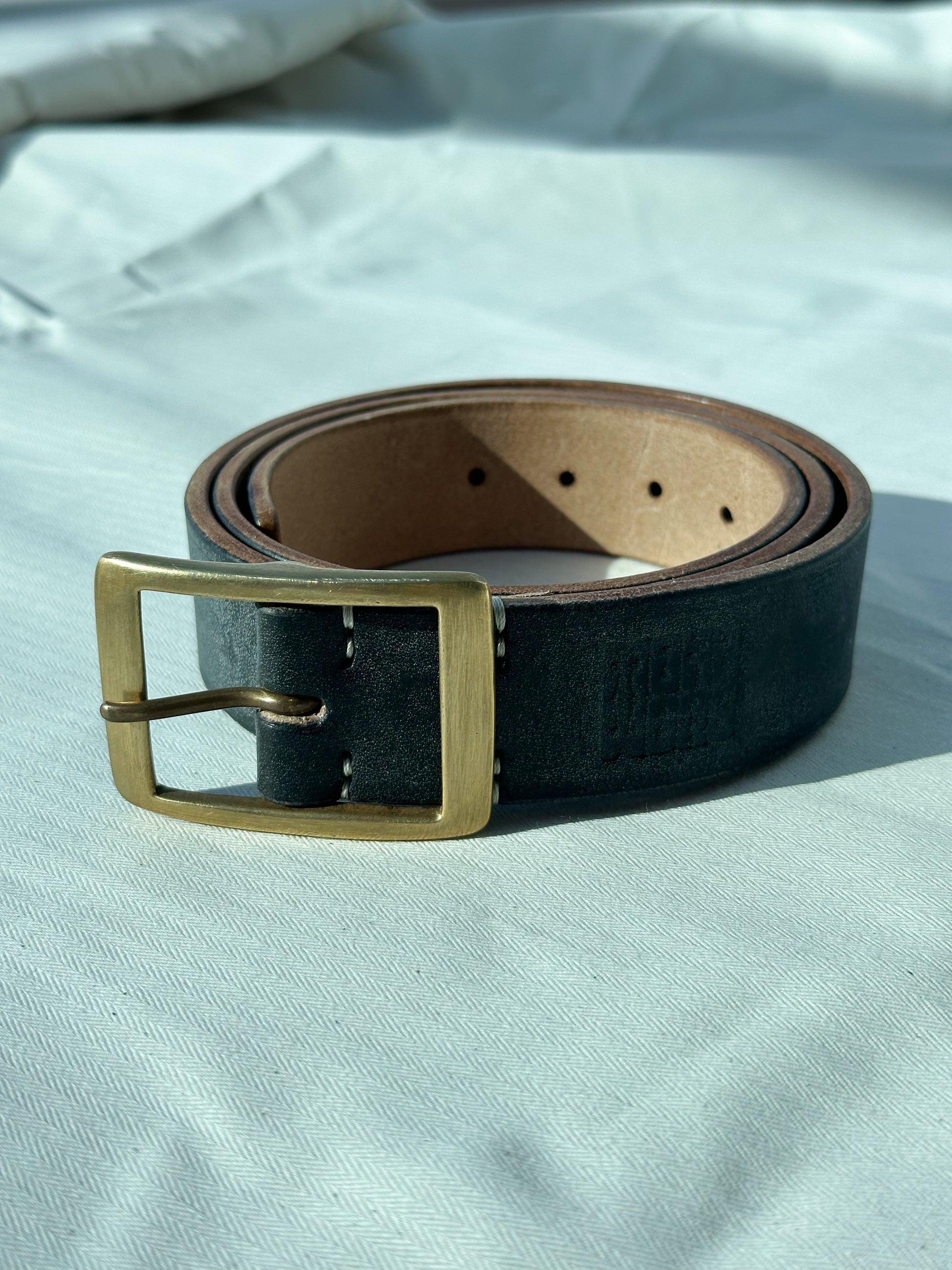 Black leather belt with a gold buckle on a light gray background