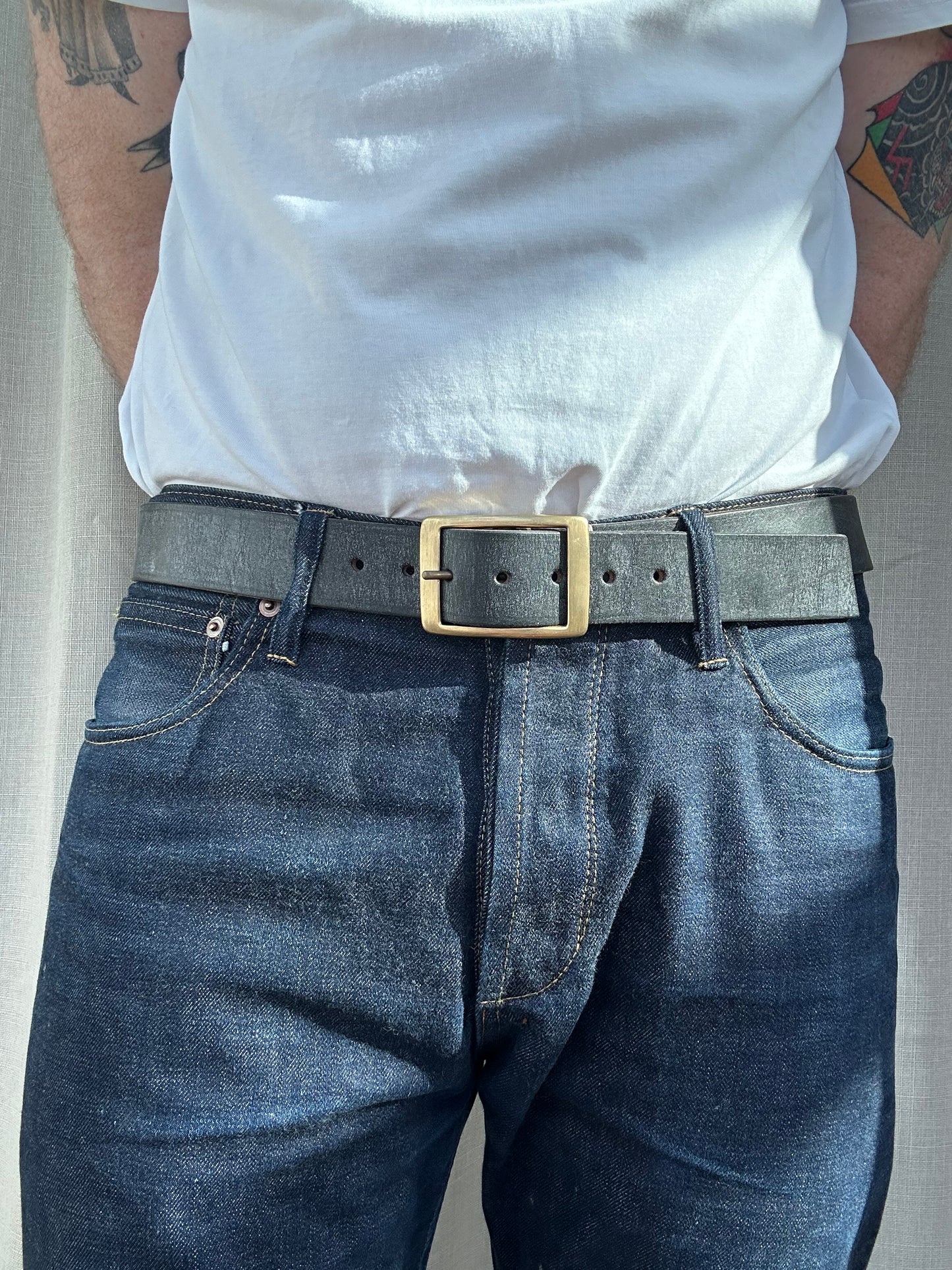 Person wearing blue jeans with a gold belt buckle on a neutral background