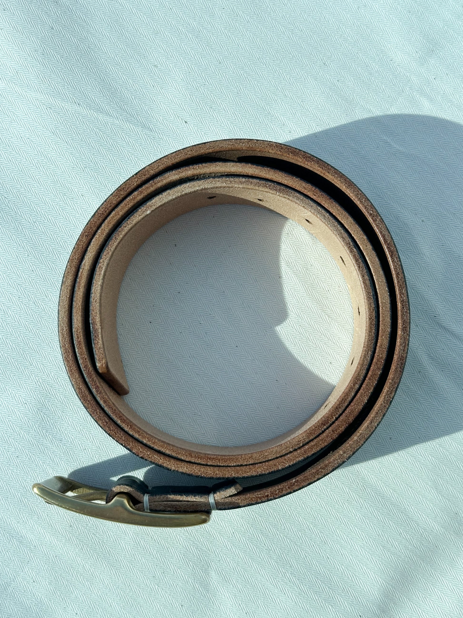Brown leather belt with a metal buckle on a light blue background